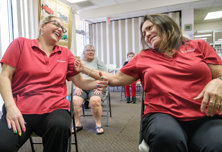 Two women in red shirts sit next to each other and raise their arms as they laugh.