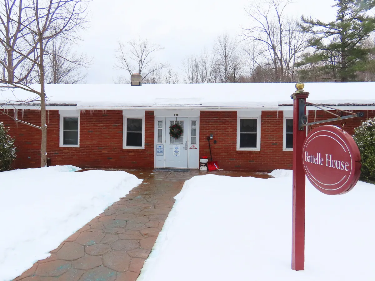 A brick building with snow on the roof and ground, carpet at the door, and a red sign reading "Battle House" at the door