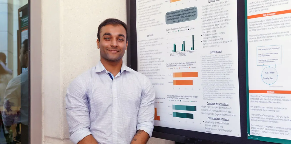 Akash Patel stands next to a research poster displayed on the wall, with charts, graphs, and text panels depicting study methods and results related to a medical or health science topic.