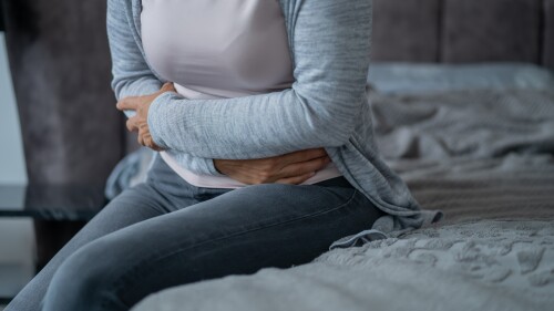 A woman experiences abdominal pain that holds her stomach while sitting