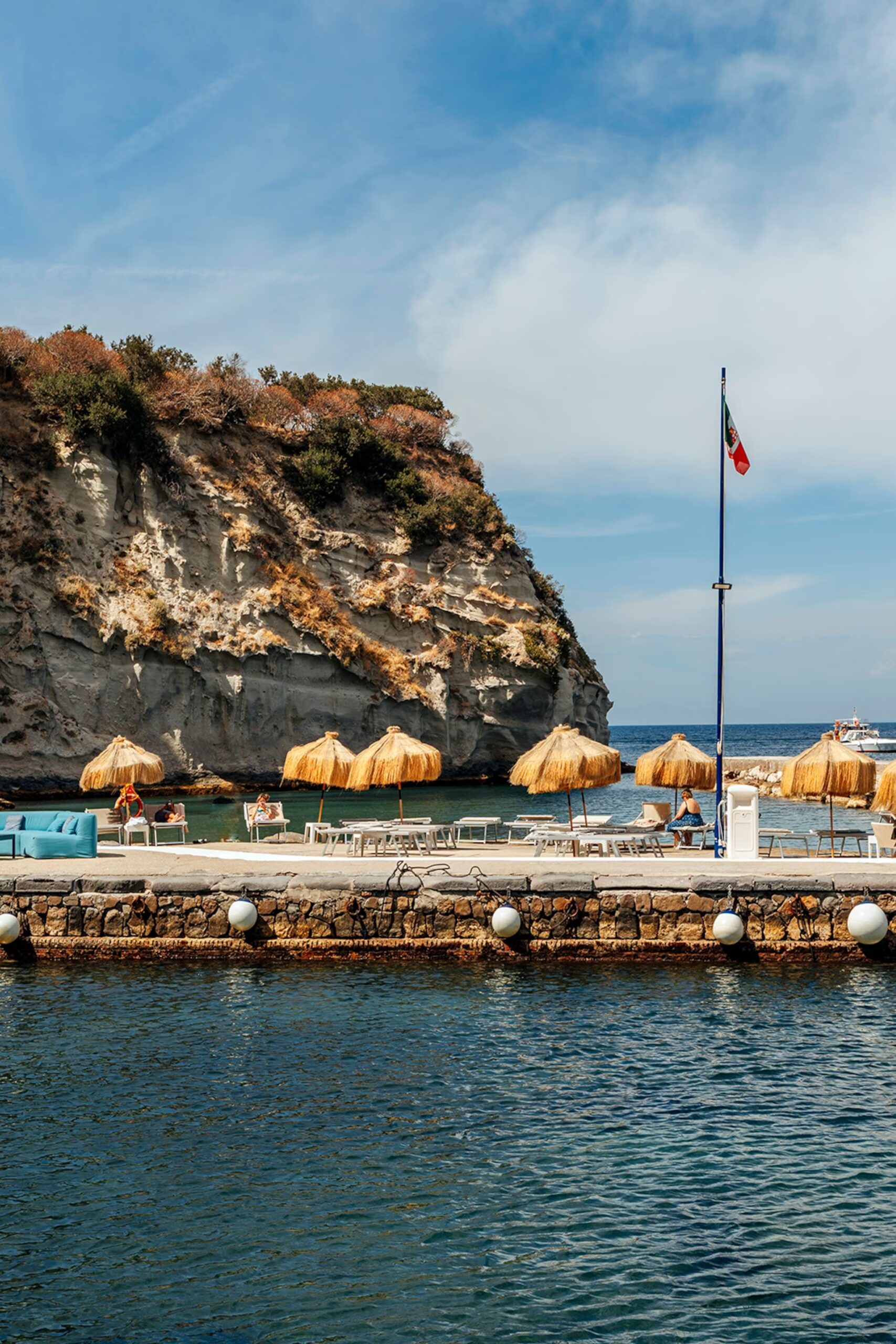 A concrete boardwalk with sun loungers and parasols leads down to the sea below.