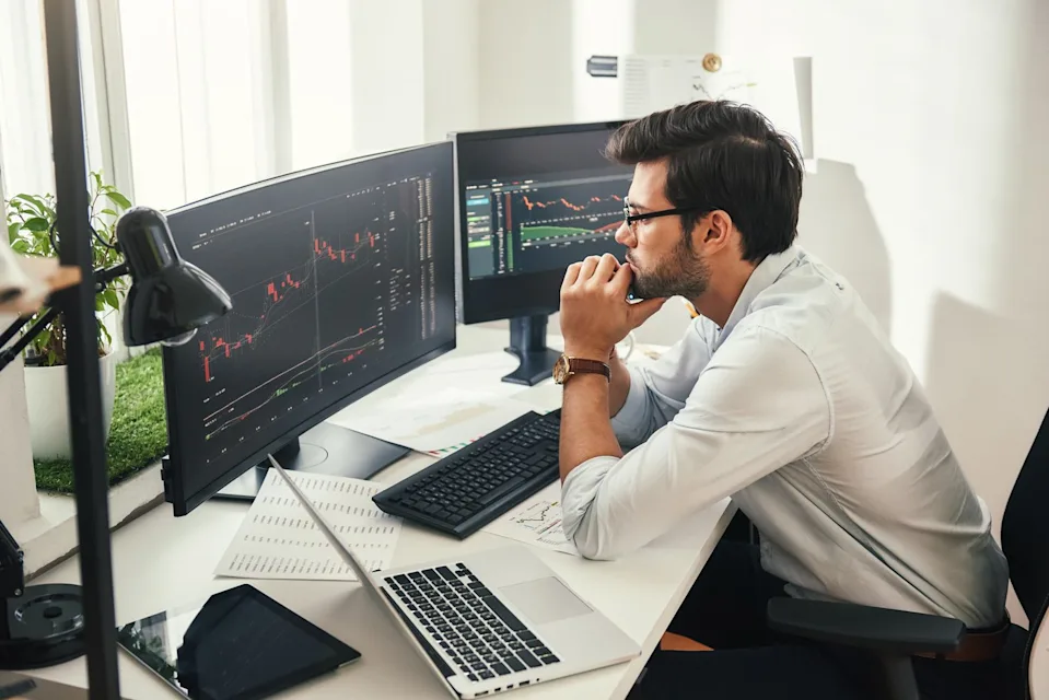 A man sitting at a desk looks at two monitors.