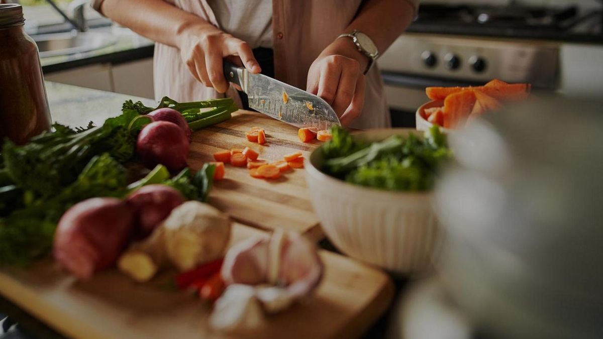 A woman cuts vegetables on a wooden board.